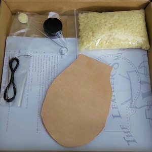 May include: A leatherworking kit with a piece of leather, a pattern, a spool of thread, a small jar of beeswax, a small bag of beads, and instructions. The kit is in a cardboard box.