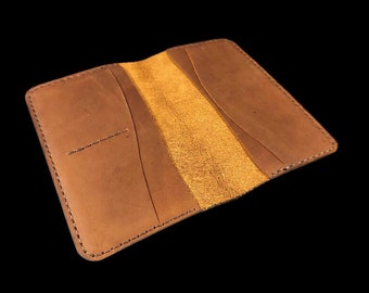 May include: A brown leather wallet with a fold-over design and a suede interior. The wallet has multiple card slots and a bill compartment.