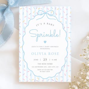 Peut inclure: Une invitation à une baby shower avec un nœud bleu clair et des accents floraux. L'invitation présente le texte "It's a Baby Sprinkle!" dans une police décorative, ainsi que les détails de l'événement. Le fond a un motif à rayures avec des vermicelles colorés.