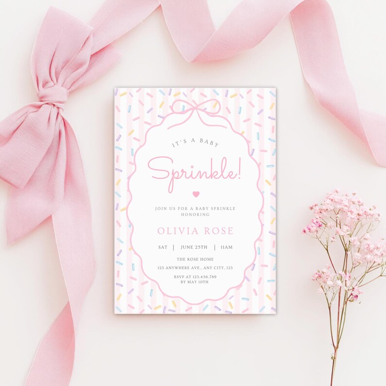 Op de afbeelding: Een baby sprinkle uitnodiging in roze en wit. De uitnodiging heeft de tekst "It's a Baby Sprinkle!" in een decoratief lettertype, met evenementdetails. Roze lint en bloemen zijn rond de uitnodiging gerangschikt.
