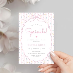 Op de afbeelding: Een baby sprinkle uitnodigingskaart met een roze en witte gestreepte achtergrond en kleurrijke confetti sprinkles. De kaart bevat de tekst "It's a Baby Sprinkle!" in een decoratief lettertype, samen met evenementdetails.
