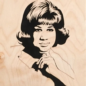 Op de afbeelding: Zwart-wit silhouet portret van een vrouw met kort haar, die een overhemd met kraag draagt, met haar handen voor haar gevouwen. Het portret is op een lichte houten achtergrond.
