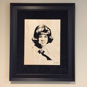 Op de afbeelding: Zwart-wit silhouet portret van een vrouw met kort haar, ingelijst in een zwart frame met een zwarte passe-partout.