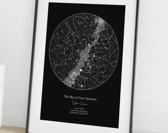May include: A framed black and white print displaying a star map. The artwork shows a circular representation of the night sky, with constellations and a bright band. The text on the print reads "The Sky of Your Moment" and includes a date and location.