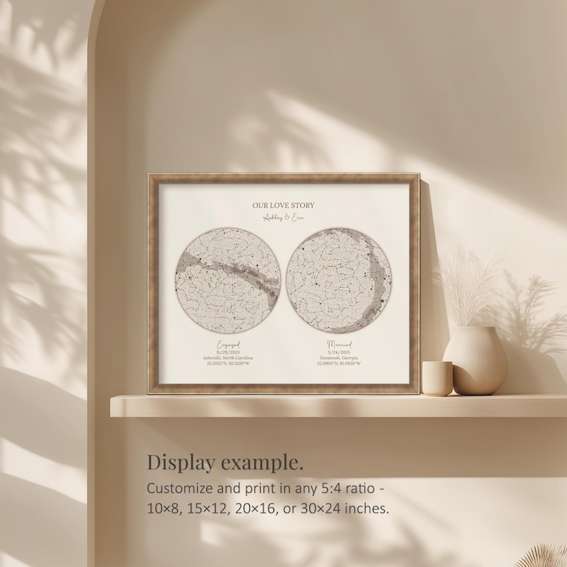 May include: Framed print with a celestial map design. The print features two circular star charts, labeled "Engaged" and "Married", with the text "Our Love Story" above. The frame is a light brown color. The print is displayed on a shelf.