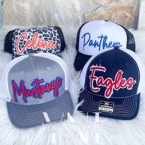May include: Four different trucker hats with various embroidered designs. The hats are white and black with a mesh back. The designs include "Celina", "Panthers", "Mustangs", and "Eagles".