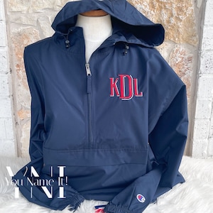 May include: A navy blue hooded jacket with a zipper closure and a white Champion logo on the left sleeve. The jacket has a red embroidered monogram "KDL" on the front.