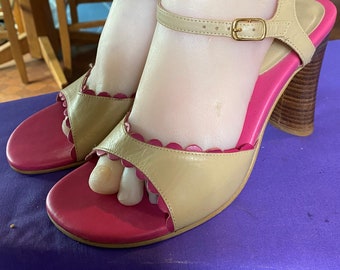 May include: Beige and pink high-heeled sandals with a scalloped edge design. The sandals have a strap around the ankle and a wooden heel. The sole is pink, and the upper is beige.