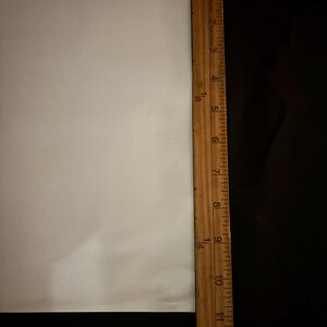 May include: A wooden ruler with inch markings, measuring up to 12 inches, is positioned vertically next to a white surface. The ruler is brown with black markings. The background is black.