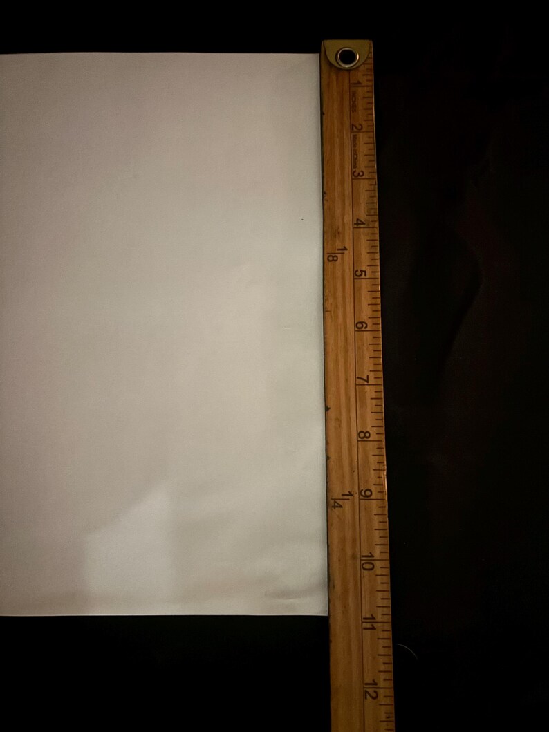 May include: A wooden ruler with inch markings, measuring up to 12 inches, is positioned vertically next to a white surface. The ruler is brown with black markings. The background is black.