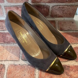 May include: A pair of gray suede Hess Couture flats with dark olive green patent leather toe caps and gold trim. The shoes have a low heel and a pointed toe. The interior of the shoe is a light tan color with gold lettering.