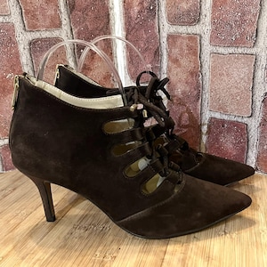 May include: A pair of brown suede ankle boots with a pointed toe and stiletto heel. The boots feature a lace-up design and a gold zipper on the back. The heel measures approximately 3 inches.