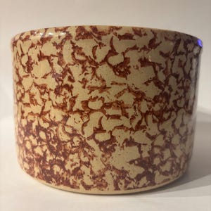 May include: A cylindrical ceramic container with a beige base and a brown, mottled pattern. The rim is slightly flared. The container has a rustic, vintage aesthetic.