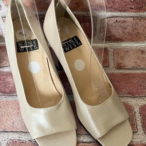May include: A pair of off-white leather peep-toe heels with a block heel. The shoes are labeled "Nine West".