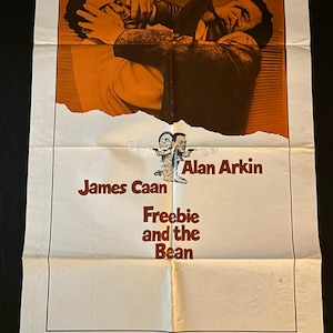 May include: Vintage movie poster for "Freebie and the Bean" featuring James Caan and Alan Arkin. The poster has an orange and brown color scheme with the film's title and actors' names prominently displayed.