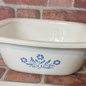 May include: White ceramic baking dish with a blue floral design. The dish has a rounded bottom and a slightly flared rim.