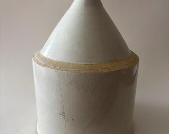 May include: A cylindrical ceramic jug with a tapered neck and a small circular opening at the top. The vessel features a smooth, off-white glazed finish with a visible vertical crack running down the side and a tan-colored band at the shoulder.
