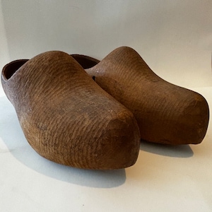 May include: A pair of brown wooden clogs. The clogs are made of a single piece of wood and have a simple, rounded shape.