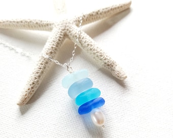 May include: A silver chain necklace with a stack of blue sea glass beads and a single white pearl charm. The necklace is displayed on a white starfish.