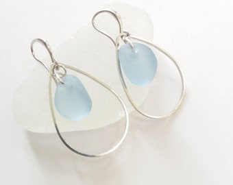 May include: A pair of silver teardrop earrings with a light blue sea glass charm hanging from each earring.