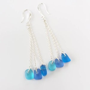 May include: Silver dangle earrings with three chains and blue glass beads. The beads are graduated in size and shade, from light blue to dark blue.