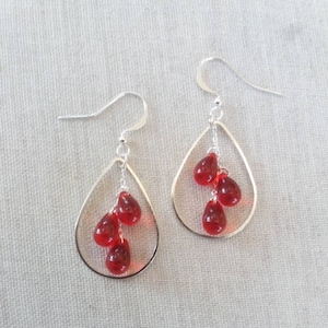 May include: Silver dangle earrings with a teardrop shape and red glass beads.