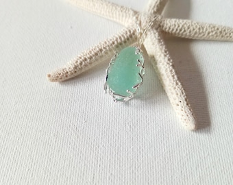 May include: A seafoam green pendant necklace with a silver-colored bezel, displayed on a white starfish. The pendant has a teardrop shape and a delicate, openwork frame. The necklace chain is also silver-colored.