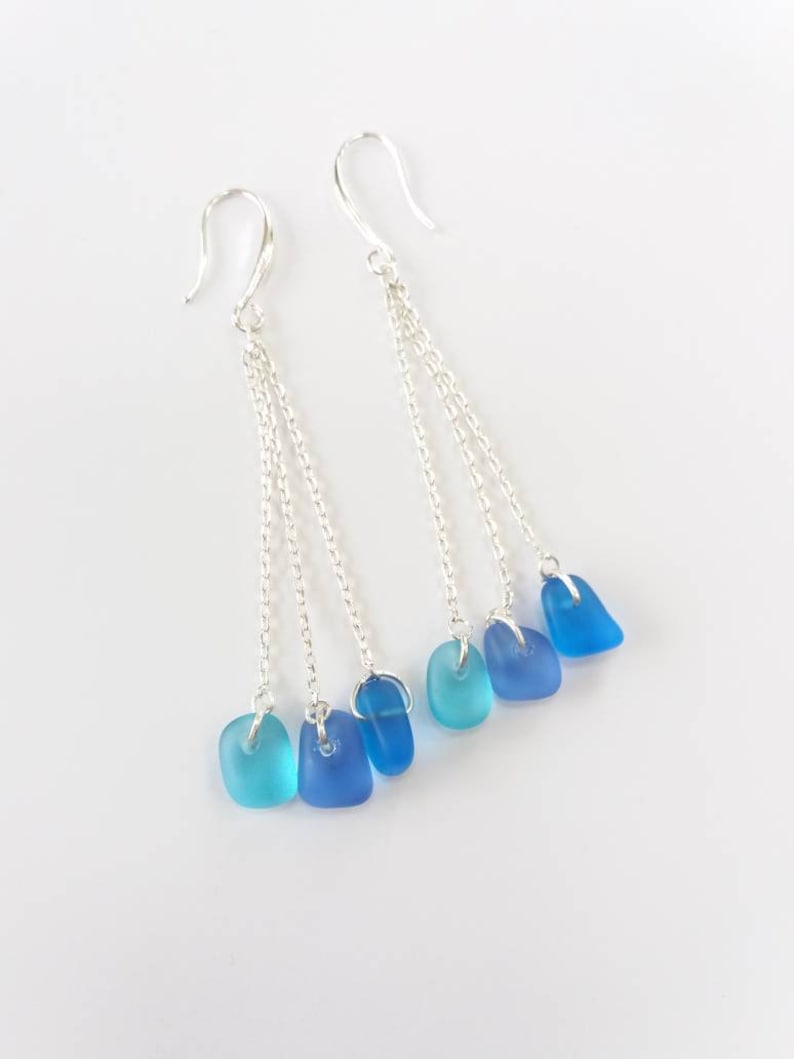 May include: Silver dangle earrings with three chains and blue glass beads. The beads are graduated in size and shade, from light blue to dark blue.