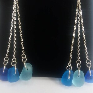 May include: A pair of silver dangle earrings with three blue sea glass charms on each earring.