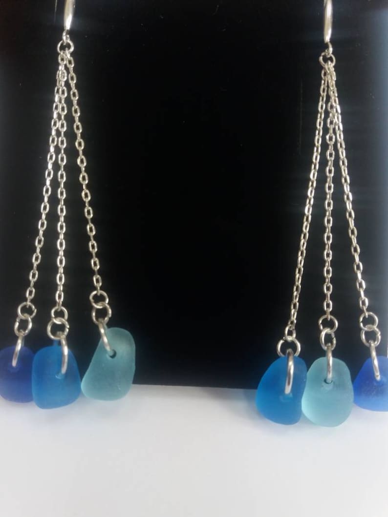 May include: A pair of silver dangle earrings with three blue sea glass charms on each earring.