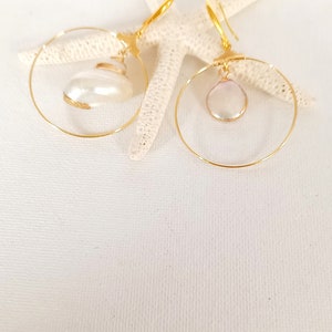 May include: A pair of gold hoop earrings with a white pearl pendant on each hoop.