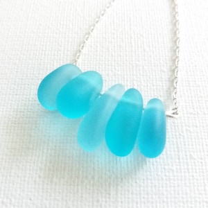 May include: A silver chain necklace with a cluster of five smooth, frosted turquoise blue sea glass beads.