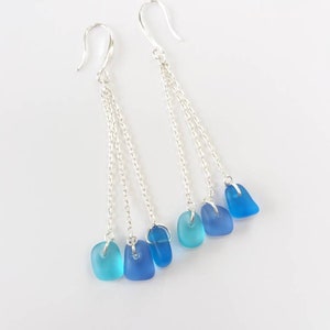 May include: A pair of silver dangle earrings with three chains each. Each chain has a blue glass bead at the end, with the beads graduating in color from light blue to dark blue.