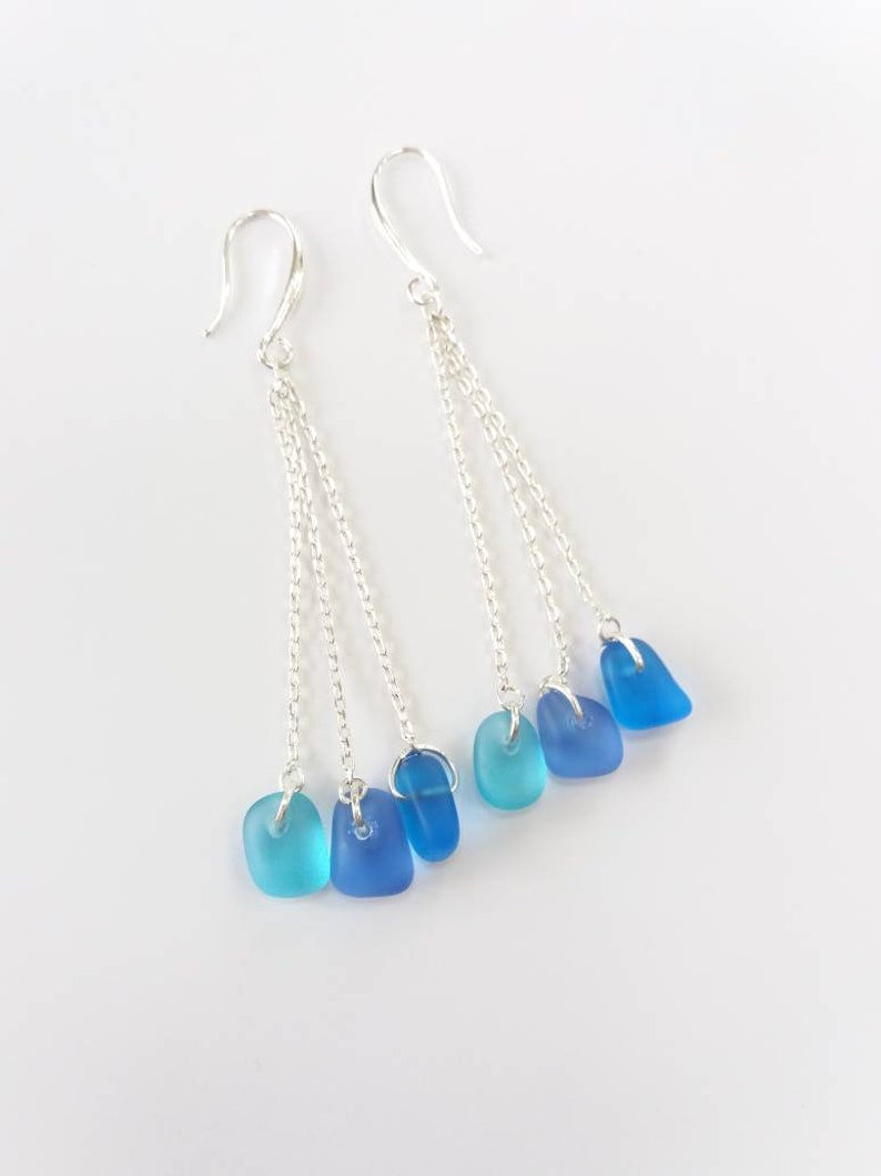 May include: A pair of silver dangle earrings with three chains each. Each chain has a blue glass bead at the end, with the beads graduating in color from light blue to dark blue.