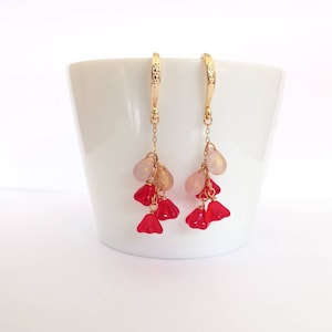 May include: Gold hoop earrings with a dangling chain of pink and red glass beads. The beads are shaped like hearts and teardrops.