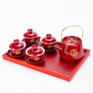 May include: A red tea set with a teapot, four teacups with lids, and saucers, all on a matching red tray. The teapot has a gold handle and a gold emblem. The teacups and saucers also have gold emblems. The set is designed for tea service.