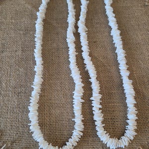 May include: Two necklaces made of small, white, irregularly shaped shell chips strung together. Each necklace features a continuous strand of white shell fragments with a metallic clasp visible at the top of each loop, creating a uniform appearance.