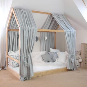 May include: A light wood-framed bed with a house-shaped canopy. The canopy features light gray curtains tied back with butterfly accents. The bed is furnished with white bedding, decorative pillows, and a star-shaped pillow.