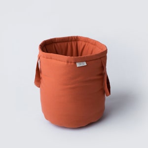Pode incluir: Uma cesta de armazenamento de tecido cor terracota com duas alças e um pequeno rótulo branco que diz "Loopy Lou".