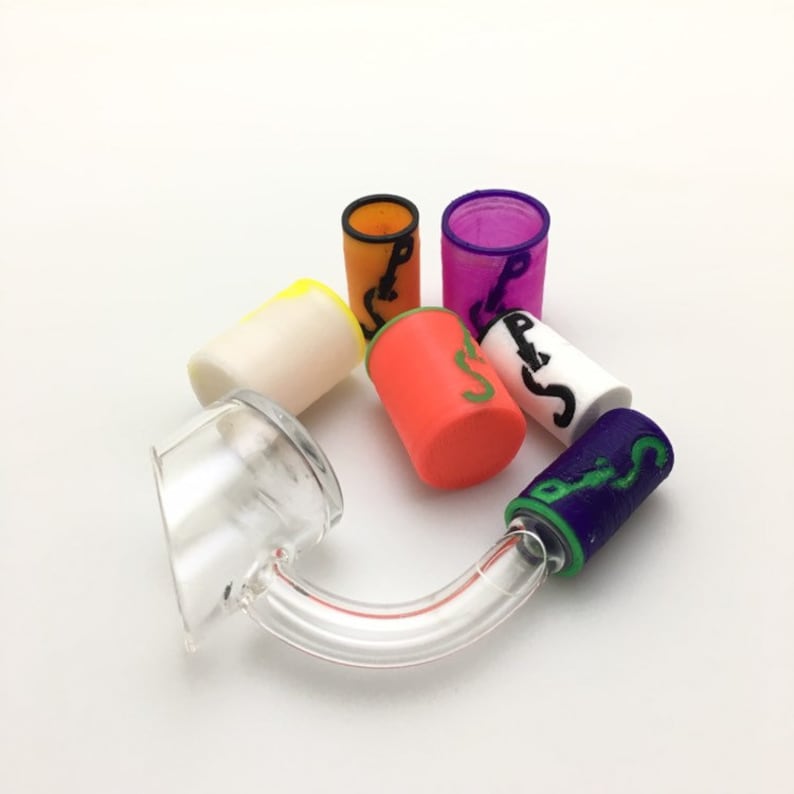 May include: A clear glass rig with a curved neck and a bowl. Surrounding the rig are several colorful silicone caps in orange, purple, white, red, yellow, and blue. Each cap has a unique design in a contrasting color.