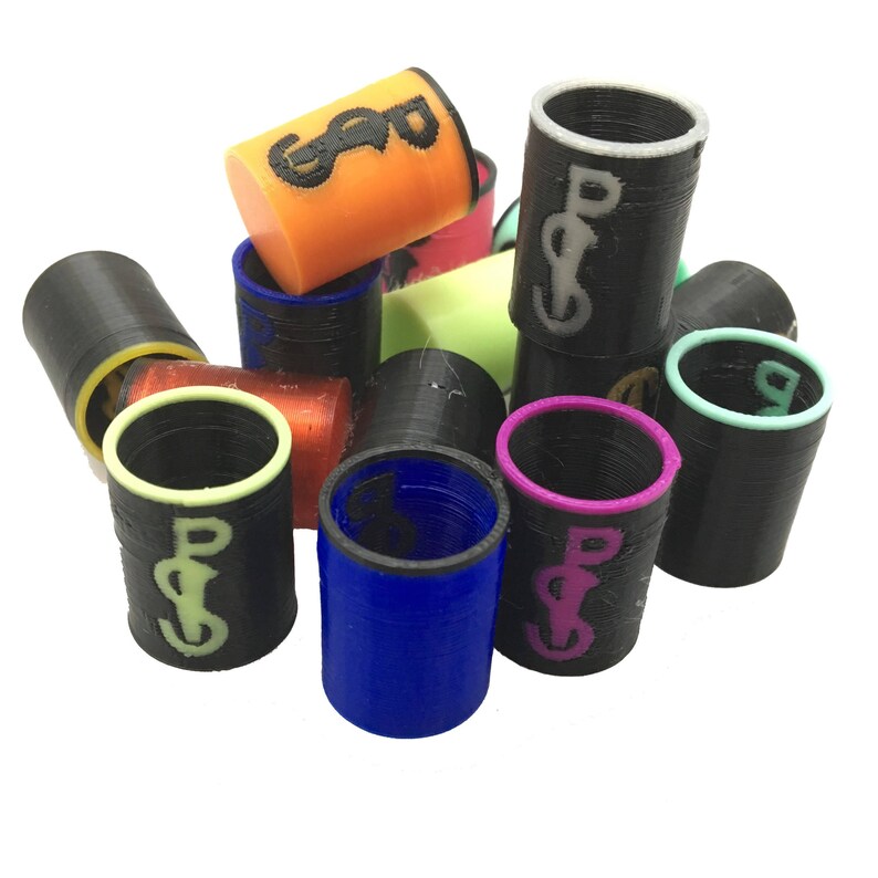 May include: A collection of cylindrical objects in various colors, including black, orange, blue, and pink. Each cylinder has a contrasting rim and a stylized graphic. The objects appear to be 3D-printed and are scattered against a white background.
