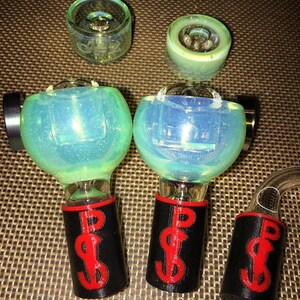 May include: A collection of glass smoking accessories. The set includes several clear glass bowls and a curved glass tube. The bowls have a blue and green iridescent finish. The bases are black with a red dollar sign design.