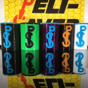 May include: A collection of cylindrical objects in various colors, including black, green, purple, orange, and white. Each cylinder features a contrasting blue or black "Peli-Saver" logo. The background displays a yellow honeycomb pattern with the text "Peli-Saver".