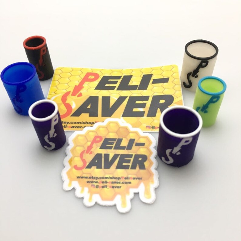 May include: A collection of colorful cylindrical accessories, each with a contrasting rim and the letters "PS". The accessories are in various colors, including blue, black, purple, green, and cream. Two stickers with the text "PELI-SAVER" are also present.