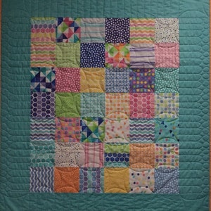 May include: A turquoise blue quilt with a white border and a patchwork design. The quilt is made up of squares of different fabrics with various patterns, including polka dots, stripes, and geometric shapes. The quilt is quilted with a curved design.