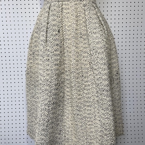 May include: A high-waisted, knee-length skirt featuring a textured, speckled knit pattern in black and off-white. The garment has a structured waistband and subtle pleats that create a flared, A-line silhouette, providing a consistent, woven appearance throughout the fabric.