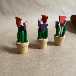 May include: Three wooden tulip flower arrangements in small pots. Each arrangement has three tulips in shades of pink, purple, and red. The tulips are painted with green leaves and stems.