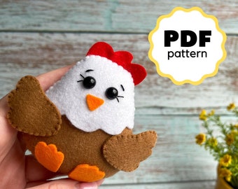 Könnte beinhalten: Ein Filz-Hühner-Spielzeug mit braunen Flügeln, orangefarbenen Füßen und einem weißen Körper mit schwarzen Augen und einem orangefarbenen Schnabel. Das Huhn hat einen roten Kamm auf dem Kopf. Das Bild enthält den Text "PDF pattern".