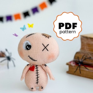 May include: A PDF pattern for sewing a cute, stitched-up doll with a single eye, a stitched-up heart, and a stitched-up X on its forehead. The doll is made of felt and has a pink blush on its cheeks.
