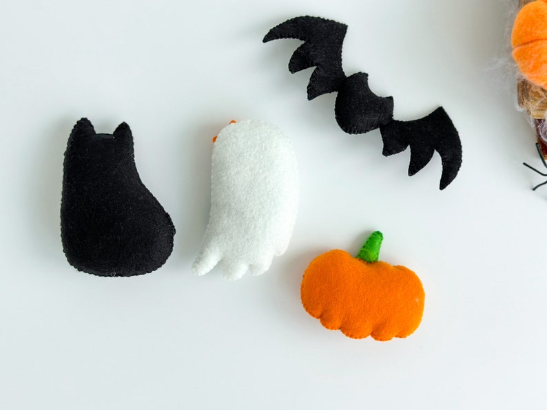 May include: A set of felt Halloween decorations including a black cat, a white ghost, an orange pumpkin, and a black bat.